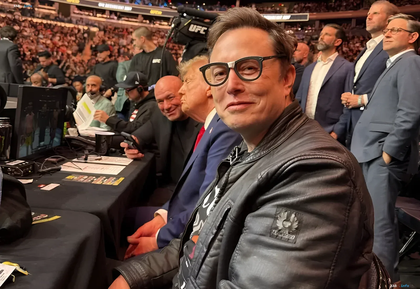 Илон Маск в очках и кожаной куртке на мероприятии UFC, рядом с Дональдом Трампом — иллюстрация к статье о рекордной компенсации Tesla
