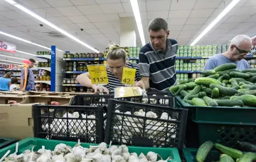 Покупатели в российском супермаркере изучают цены на овощи и грибы, что иллюстрирует рост стоимости жизни и социальный кризис, предсказанный экономистом ВЭБ.РФ