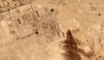 Satellite image of an Iranian oil complex with smoke from an explosion, illustrating conflict escalation and allies' doubts about US protection