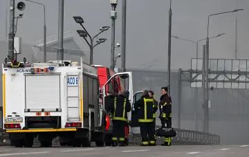Feuerwehr-Einsatzkräfte des russischen Katastrophenschutzministeriums (EMERCOM) am Ort eines Vorfalls in Moskau nach einem Drohnenangriff, Rauch im Hintergrund des Wildberries-Lagers