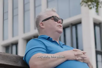 Мужчина в синей рубашке и умных очках Ray-Ban Meta сидит на скамейке, демонстрируя использование очков для слабовидящих