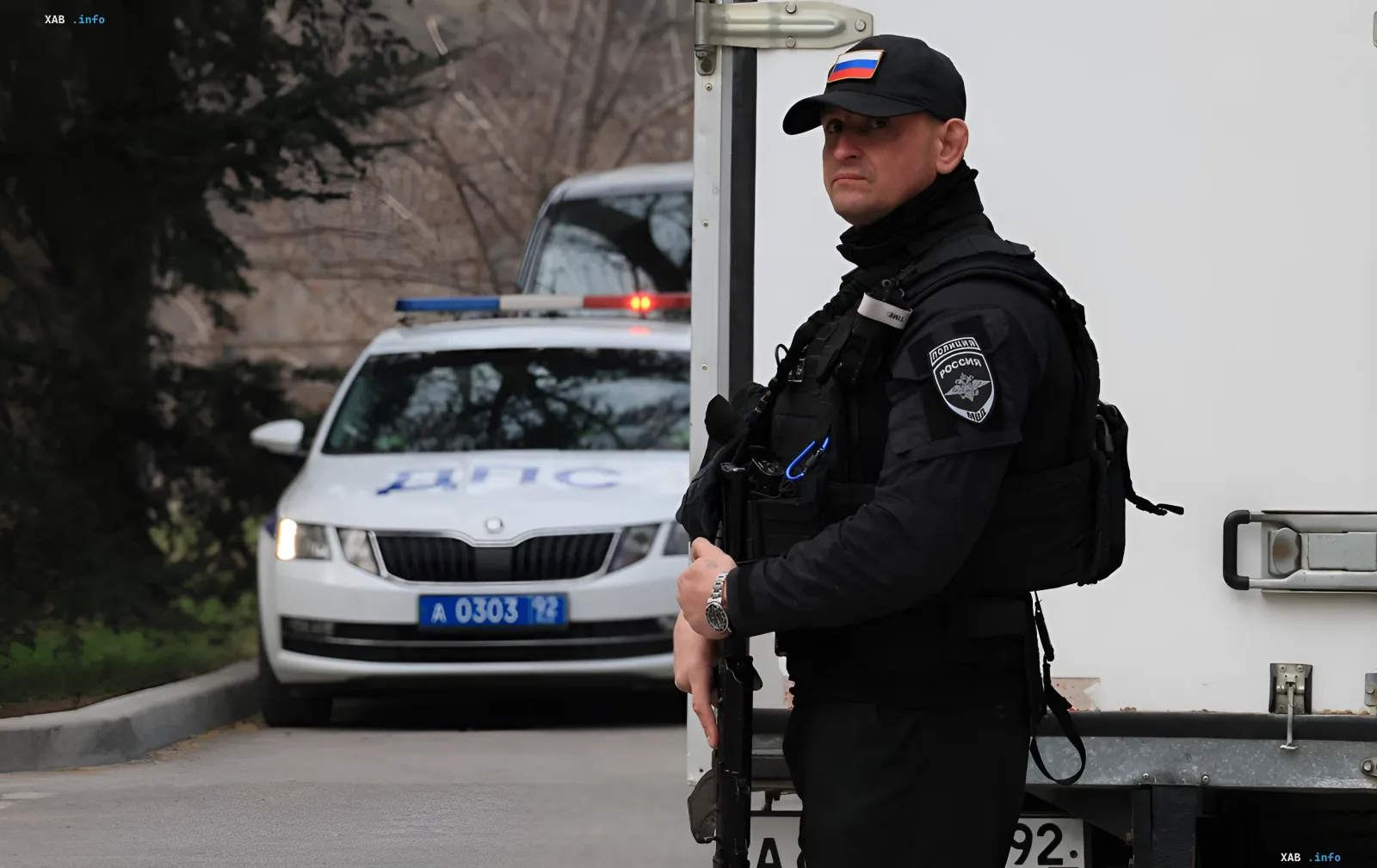 Armed police officer stands at a checkpoint on the road with a police car in the background, illustrating the increased control of movement under the new Russian Ministry of Transport decree on digital totalitarianism.