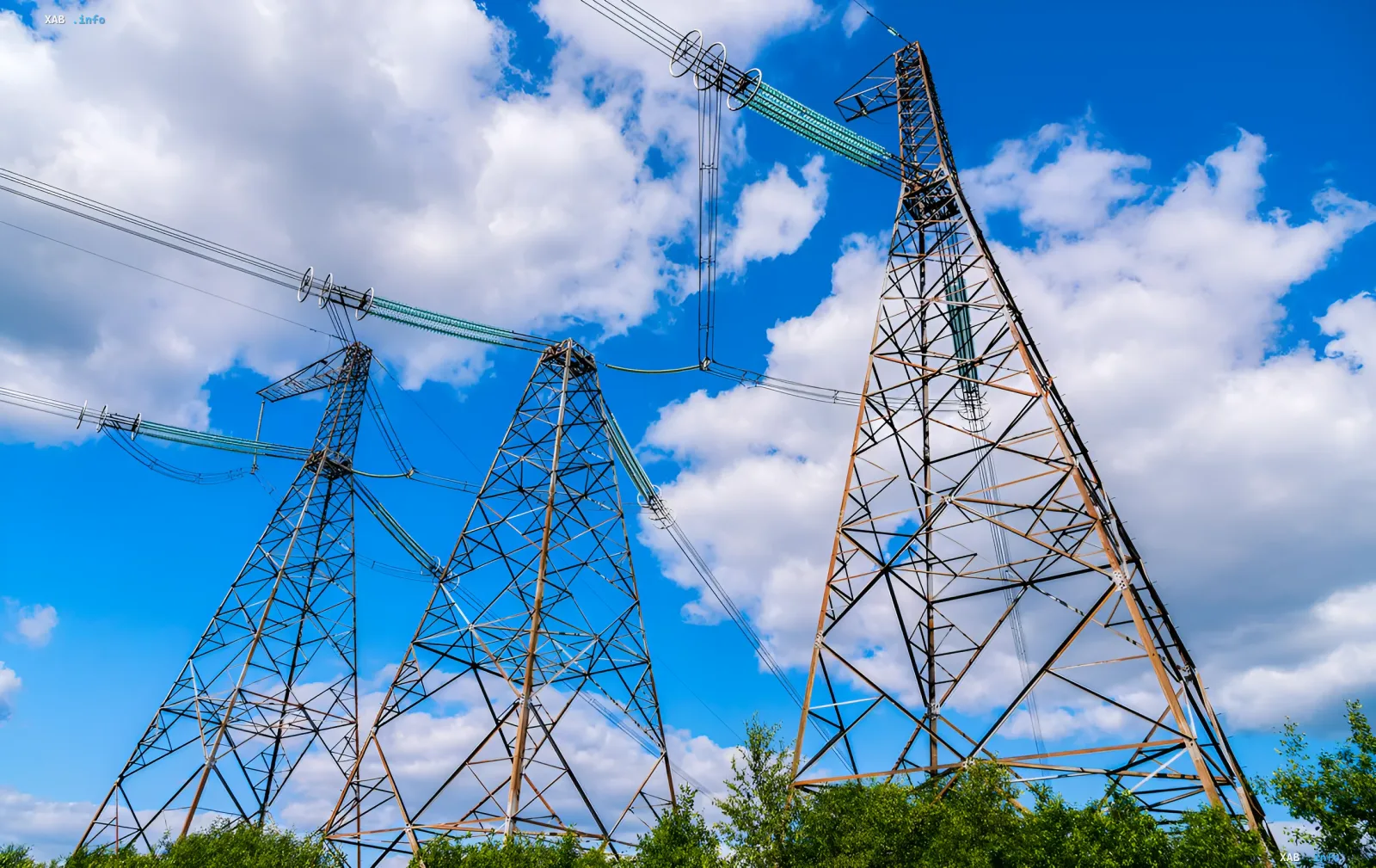 High-voltage transmission towers against a blue sky with clouds — symbolizing Ukraine’s energy grid facing a price deadlock and threats from price caps