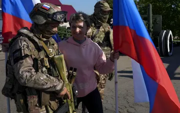 Female student in pink hoodie with Russian flag next to camouflaged soldiers, illustrating youth recruitment for TOT