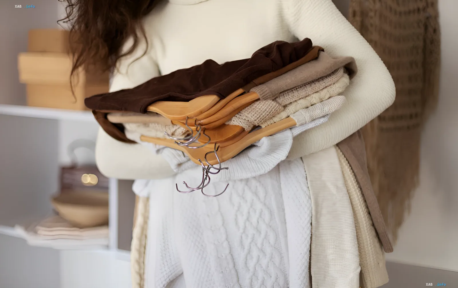Frau hält Stapel von Vintage-Pullovern auf Holzkleiderbügeln — Herbsttrend 2026, inspiriert von Omas Garderobe