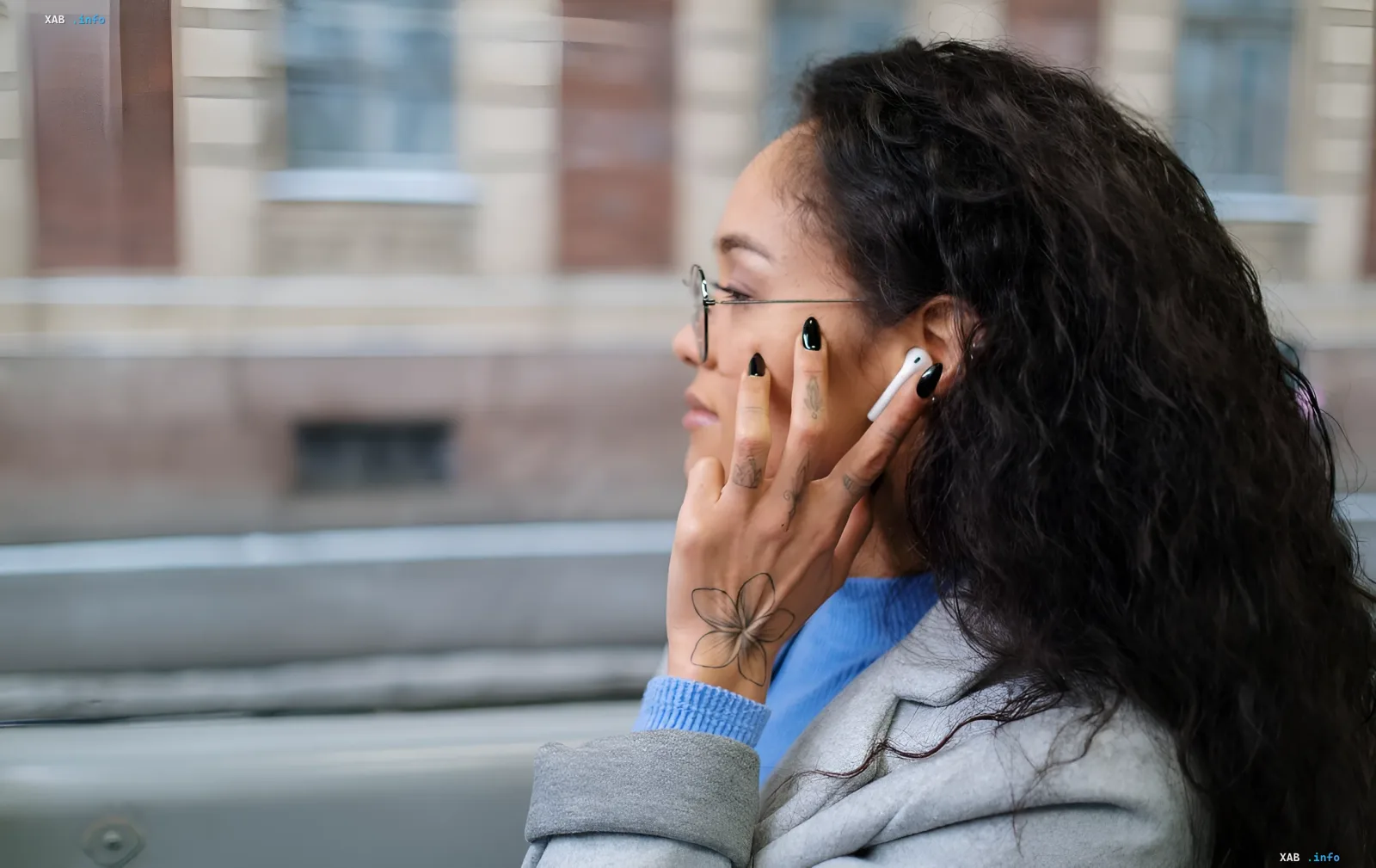 Женщина в очках с AirPods Pro в ушах смотрит в окно поезда, задумчиво касаясь наушника пальцем