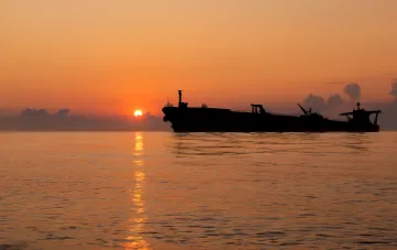 Силуэт нефтяного танкера на фоне заката в Черном море, иллюстрирующий атаку на танкер Skiros и риски для российской нефти.
