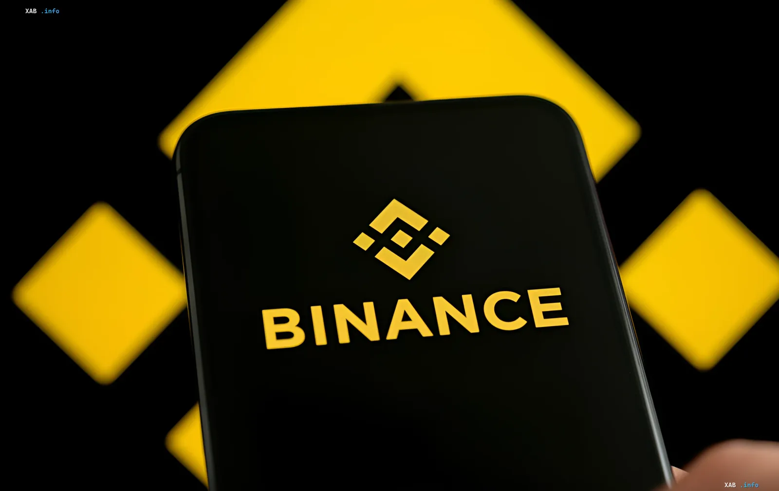 Логотип Binance на экране смартфона с желтыми геометрическими элементами на фоне — иллюстрация к новости о передаче данных о криптопожертвованиях россиян в Москву