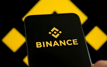 Логотип Binance на экране смартфона с желтыми геометрическими элементами на фоне — иллюстрация к новости о передаче данных о криптопожертвованиях россиян в Москву