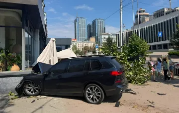 Разбитый черный BMW врезался в летнюю террасу ресторана в центре Киева, рядом стоят свидетели аварии