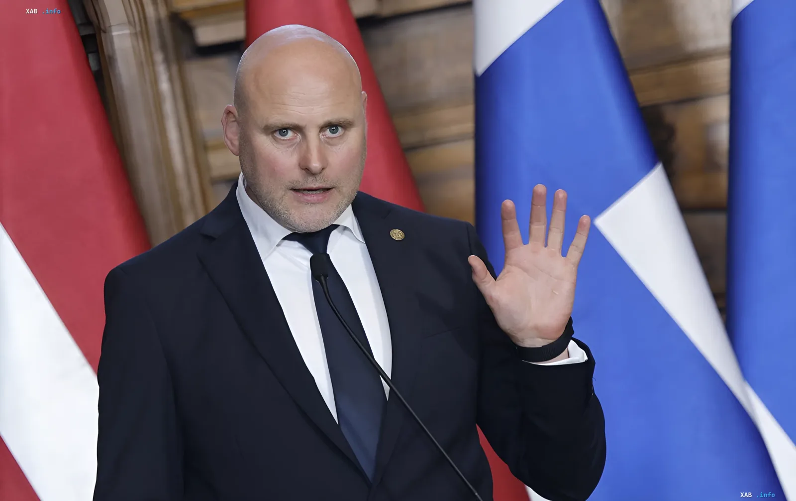 Latvian Foreign Minister Edgars Rinkēvičs speaking at a podium with Latvian and EU flags, criticizing errors in EU sanctions against Russia