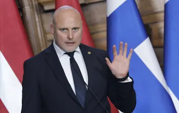 Latvian Foreign Minister Edgars Rinkēvičs speaking at a podium with Latvian and EU flags, criticizing errors in EU sanctions against Russia