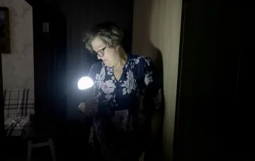 Женщина с фонариком в темной комнате после отключения электричества в Чернигове из-за атаки на энергосистему