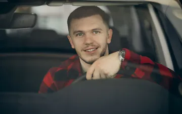 Lächelnder Mann am Steuer eines Autos, der die Möglichkeit für ukrainische Fahrer symbolisiert, in Deutschland ohne Führerscheinprüfung zu fahren
