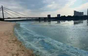 Пена на поверхности Днепра в Киеве: вид с пляжа на реку с мостом на фоне