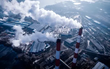 Industrielle Schornsteine mit Rauchfahnen vor winterlicher Landschaft — Symbol für den Druck der Ökosteuer auf die ukrainische Bergbauindustrie