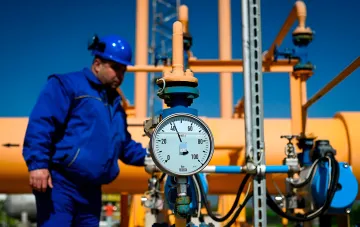 Arbeiter in blauer Arbeitskleidung und Helm überprüft Druckmesser an Gasleitung, symbolisiert Exportkontrolle und Erhaltung der ukrainischen Förderung