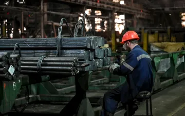 Arbeiter in Schutzausrüstung bearbeitet Stahlträger in einem metallurgischen Werk, was die Bedrohung einer Produktionsstilllegung aufgrund von Tarifen und Hafenblockaden veranschaulicht