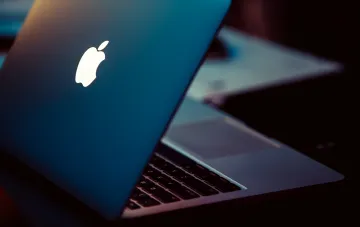 Ноутбук MacBook с логотипом Apple на фоне, символизирующий утечку информации из macOS Tahoe о новых устройствах Apple
