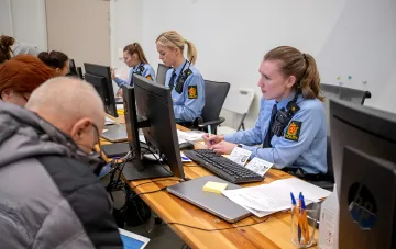 Norwegian police officers at workstations with documents and computers, illustrating administrative procedures related to the case of discrimination against a Russian scientist in Norway.