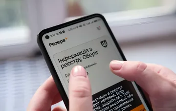 Smartphone mit der App 'Rezerv+' auf dem Bildschirm, die Daten aus dem Oberyh-Register anzeigt – Illustration der digitalen Mobilmachung und Online-Aufschub für Lehrkräfte