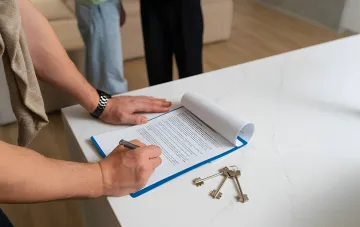 Людина підписує договір оренди квартири, поруч лежать ключі, що ілюструє важливість оформлення документів для уникнення штрафів у 2026 році