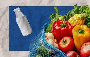 Стеклянная бутылка молока и сетка с овощами на синем фоне, иллюстрирующая изменение цен на продукты в украинских супермаркетах 18 августа