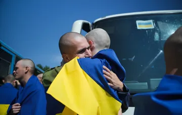 Українські військові обіймаються після повернення з полону в рамках 77-го обміну, тримаючи український прапор