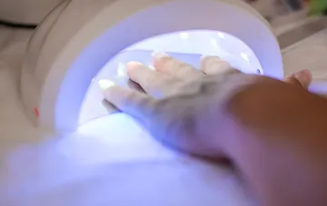 Hand in UV-Lampe zum Aushärten von Gel-Lack – Illustration zur Nachricht über das Verbot eines gefährlichen Bestandteils in Großbritannien