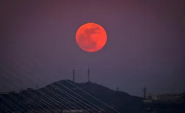 Кровавая Луна во время частного лунного затмения 28 августа: ярко-красное лунное диск на тёмном небе над силуэтом холма с вышками связи