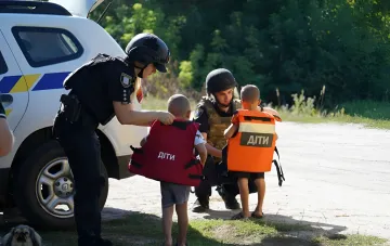 Полиция помогает детям надеть жилеты с надписью «ДІТИ» во время эвакуации из прифронтовой зоны Донецкой области
