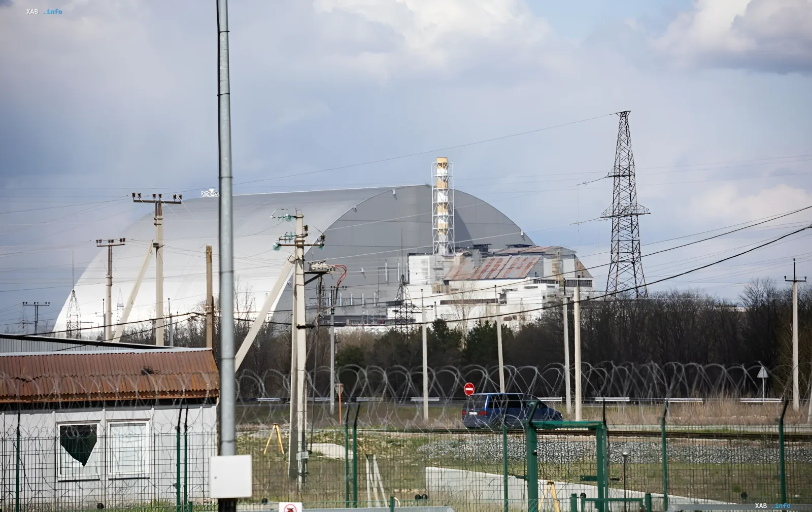 Neue sichere Einschlussstruktur (NSC) des Kernkraftwerks Tschernobyl vor einem bewölkten Himmel, umgeben von einem Stacheldrahtzaun und Stromleitungen.