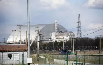 Neue sichere Einschlussstruktur (NSC) des Kernkraftwerks Tschernobyl vor einem bewölkten Himmel, umgeben von einem Stacheldrahtzaun und Stromleitungen.