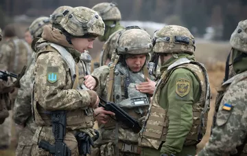 Украинские военные в камуфляжной форме обсуждают тактику, один из них держит оружие, на рукавах видны эмблемы Вооруженных сил Украины