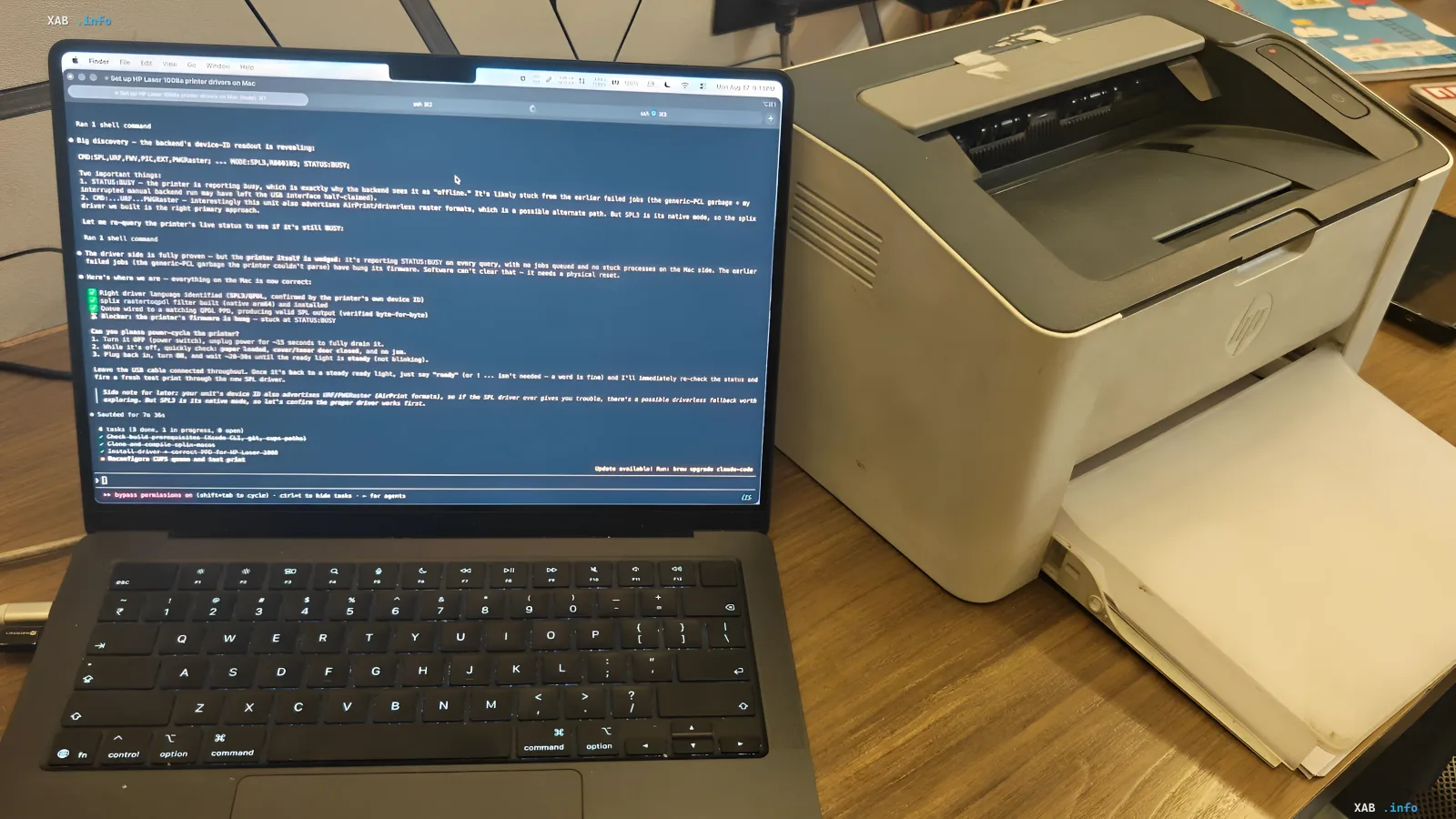 MacBook laptop with open terminal where AI Claude helps configure driver for legacy HP Laser 1008a printer on macOS