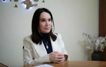 Irina Mudraya in weißem Blazer und marineblauem Rollkragenpullover, sitzt an einem Tisch während einer offiziellen Veranstaltung oder eines Interviews, erhielt Verdacht von NABU im Rahmen der Operation „Forrest Gump“