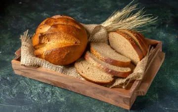 Frisches Brot in einer Holzkiste: ganzer Laib und geschnitten mit Samen, Illustration zum Artikel über die Aufbewahrung von Brot ohne Kühlschrank