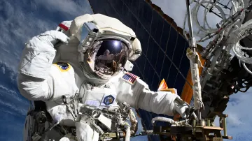 Астронавт NASA в скафандре во время выхода в открытый космос обслуживает антенное оборудование МКС на фоне солнечных панелей и Земли