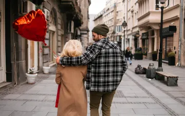 Молодая пара гуляет по улице, мужчина обнимает женщину, рядом красный воздушный шар в форме сердца — иллюстрация к статье о психологии отношений и фразах, покоряющих сердце мужчины
