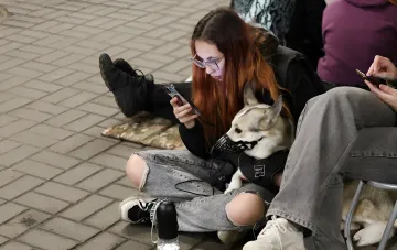 Eine Bürgerin mit einem gezähmten Hund ruht auf der Straße und wartet auf ein Alarmsignal, was das tägliche Leben unter neuen Schutzraumregeln illustriert