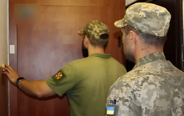 TCU-Beamte in Militäruniform überprüfen Dokumente an einer Tür und illustrieren den Mobilisierungsprozess in der Ukraine