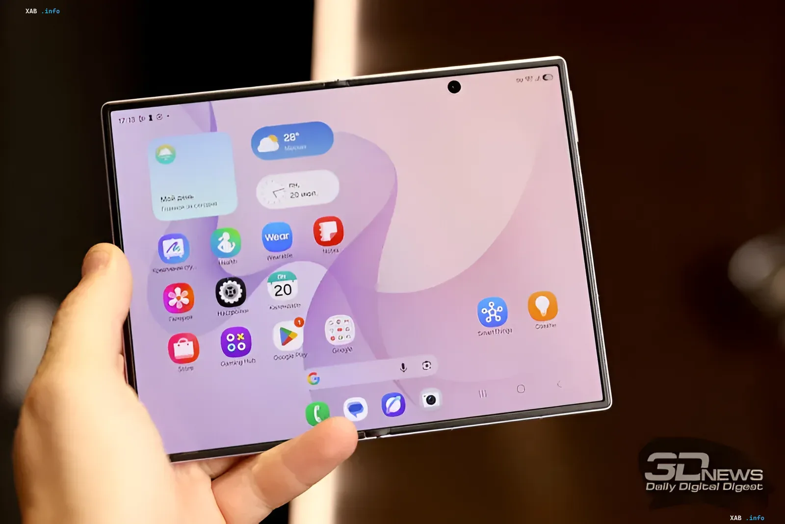 Ручка держит широкий складной смартфон Samsung с открытым экраном, демонстрирующий интерфейс One UI, что иллюстрирует грядущий Galaxy Z Fold9 2027 года