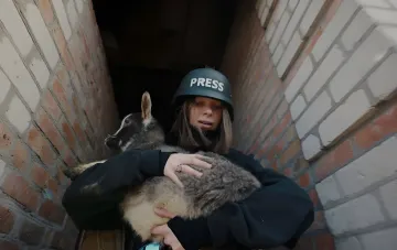 Журналістка в шоломі з написом PRESS рятує цуценя в зоні бойових дій з фільму «Спасай»