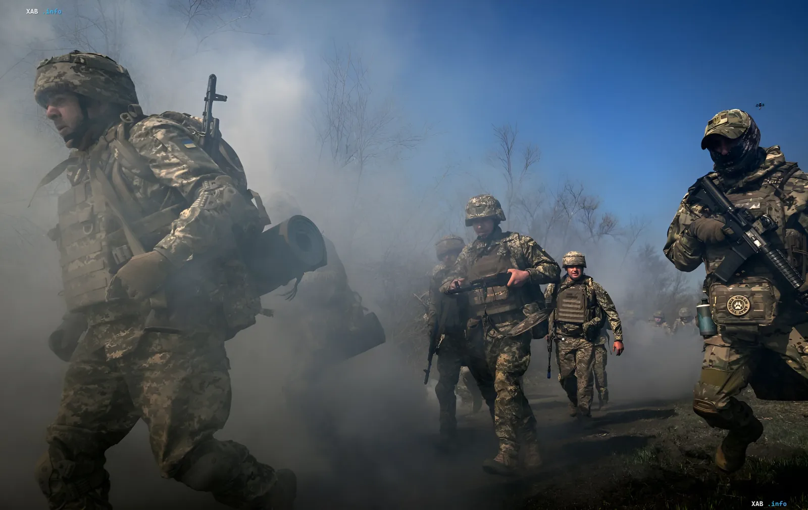 Украинские военные в камуфляже с оружием продвигаются сквозь дым на фоне голых деревьев