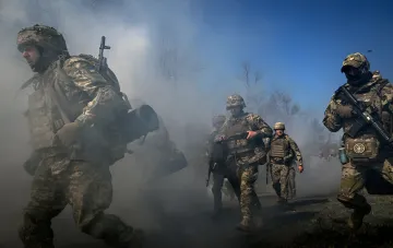 Украинские военные в камуфляже с оружием продвигаются сквозь дым на фоне голых деревьев