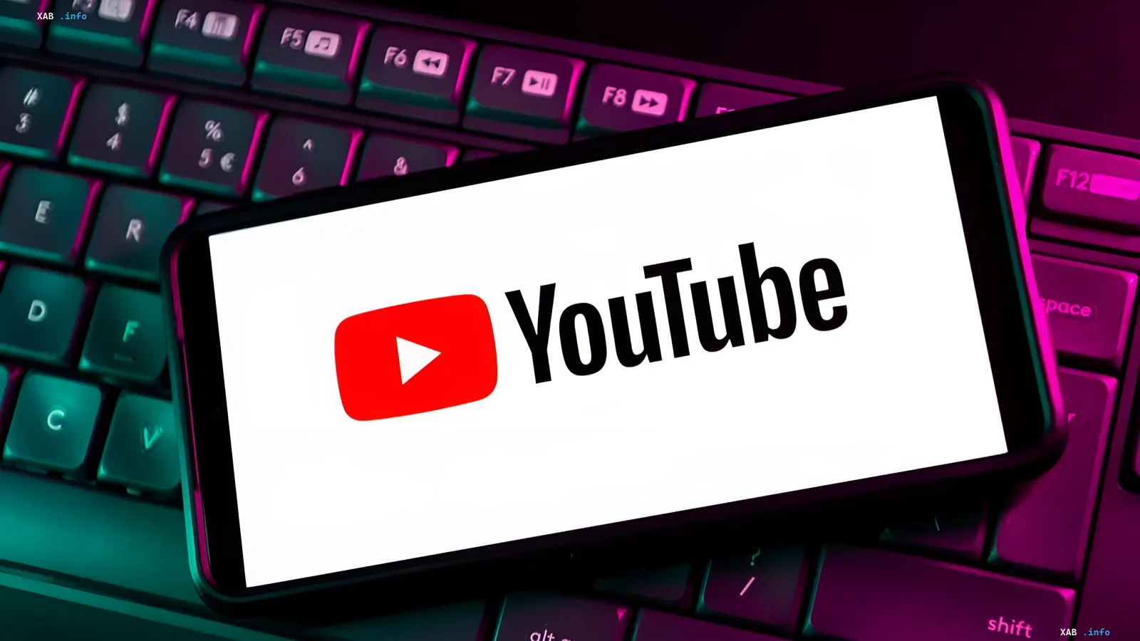 Логотип YouTube на экране смартфона, лежащего на клавиатуре с RGB-подсветкой — символ грядущих изменений в подсчёте просмотров с 24 августа 2026 года