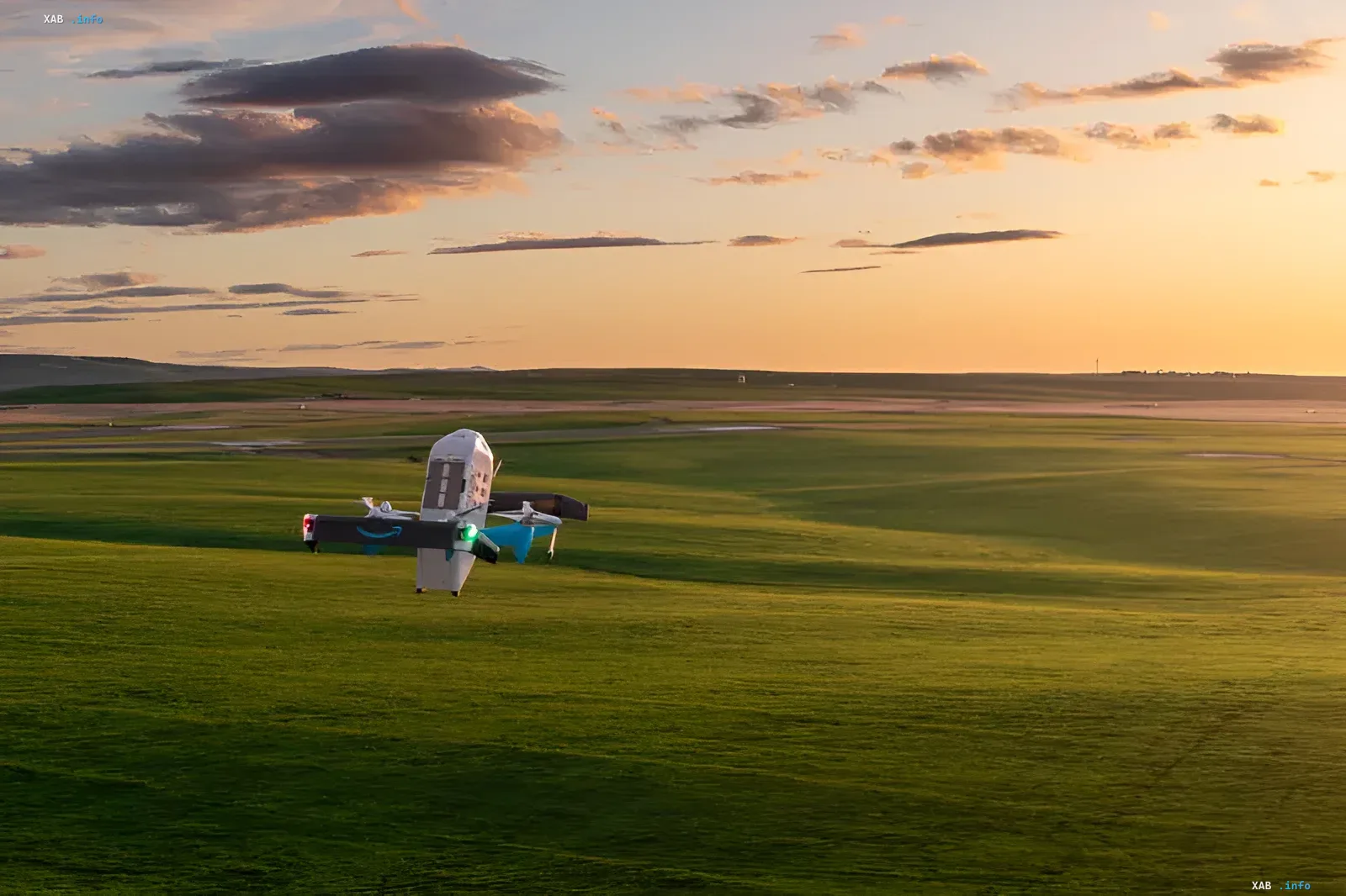 Amazon-Prime-Air-Lieferdrohne mit Firmenlogo fliegt bei Sonnenuntergang über ein grünes Feld – Drohnenlieferungen sollen bis Ende 2026 fast 500 US-Städte abdecken