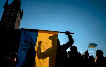Силует людини з українським синьо-жовтим прапором на мітингу в Празі на тлі старовинної вежі з годинником, протест щодо скасування тимчасового захисту для українських біженців у Чехії