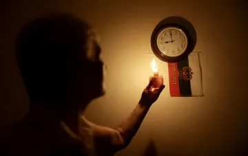 Житель тримає запалену свічку в темряві під час блекауту в Криму; на стіні годинник і російський прапор