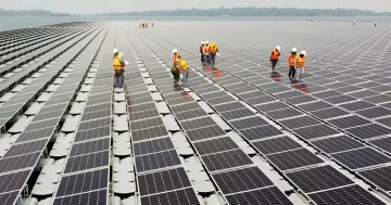 Arbeiterschutzwesten tragende Arbeiter warten Reihen von Solarmodulen auf einer großen Dachkraftwerk in Südostasien während der Energiekrise
